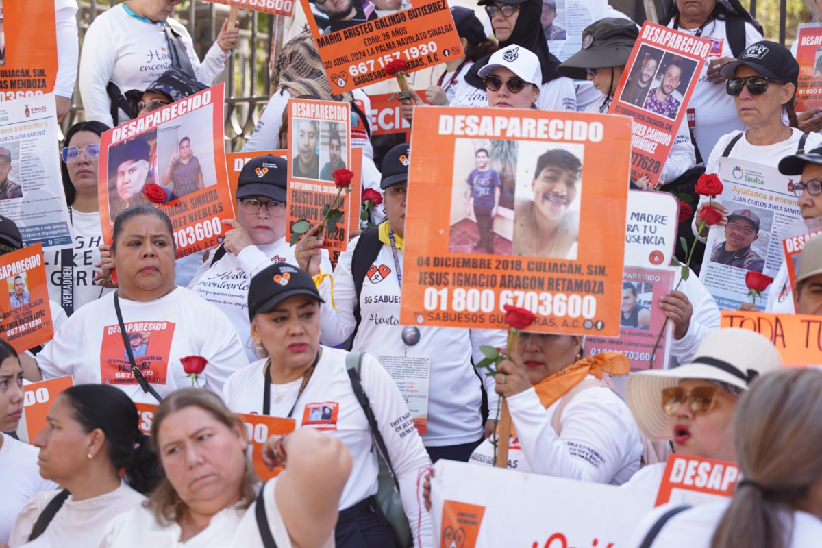 Colectivo de familiares de personas desaparecidas en Sinaloa durante una protesta, con carteles naranjas que muestran fotografías, nombres y fechas de desaparición.